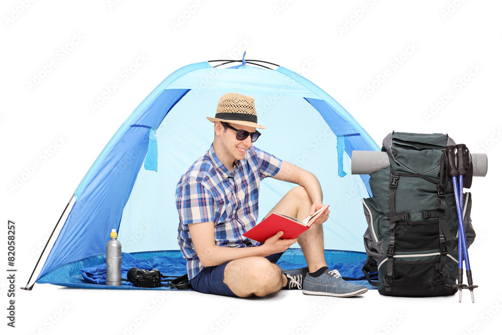 Wall mural young camper reading a book seated on the ground