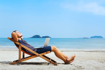 smiling businessman with computer relaxing on the beach