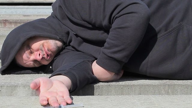Drug addict man sleeping with syringe near hand