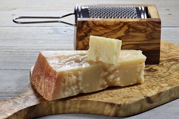 italienischer Grana Padano Käse mit Reibe und Brettchen aus Olivenholz auf Holztisch