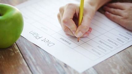 close up of young woman writing diet plan at home