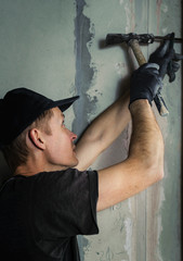 Woker hammers a nail with a foot into a wall