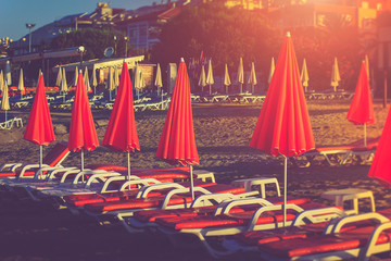 Red umbrellas and beach chairs on the beach in sunlight.
