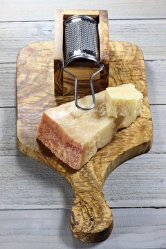 italienischer Grana Padano Käse mit Reibe und Brettchen aus Olivenholz auf Holztisch