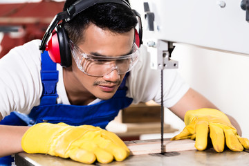 Asian carpenter or worker on saw with wood