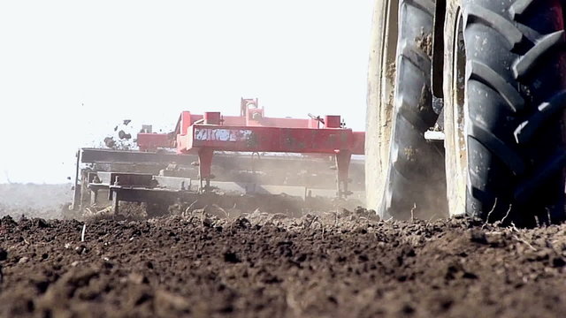Tractor pulling land cultivating machine.