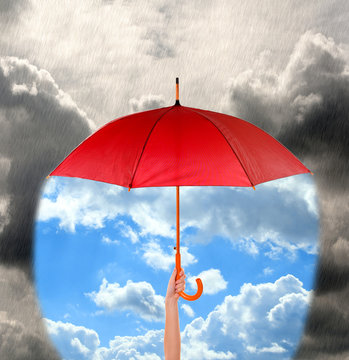 Red umbrella in hand protecting good weather from dark clouds of rain