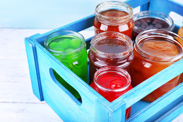 Homemade jars of fruits jam in crate on wooden table and color wall background