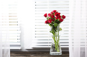 Red roses in glass vase on windowsill background