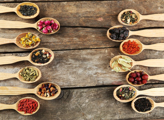 Collection of tea and natural additives in wooden spoons, on old wooden table