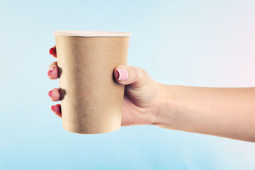 Female hand with paper cup on blue background