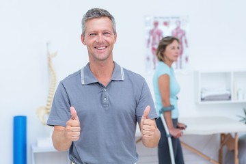 Doctor smiling at camera while his patient standing with crutch
