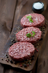 Raw beef cutlets with various spices, rustic wooden background