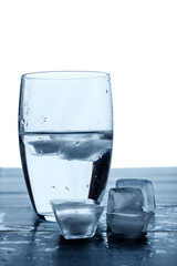 Glass of water and melting ice cubes on a wooden table.