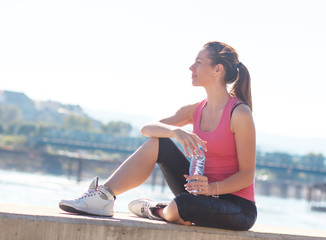 Fototapeta premium Young woman sitting on the riverbank and resting after jogging.