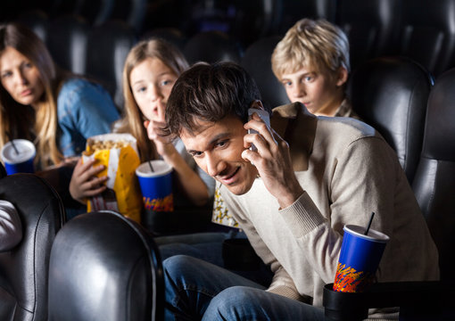 Family Looking At Man Using Mobilephone In Theater