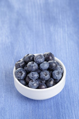 heap of fresh washed blueberries in white bowl on blue wood