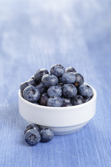 heap of fresh washed blueberries in white bowl on blue wood