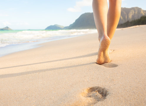 Woman walking on sandy beach leaving footprints in the sand.