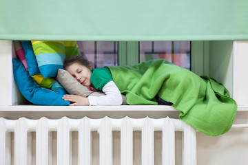 Young child sleeping on the windowsill over heating radiator