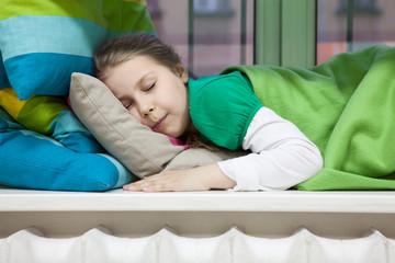 Fototapeta premium Close up of girl sleeping on window sill with bright pillows