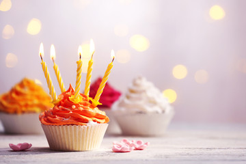 Delicious birthday cupcakes on table on light background