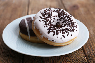 Delicious donuts with icing on plate on wooden background