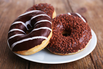 Delicious donuts with icing on plate on wooden background