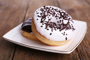 Delicious donuts with icing on plate on wooden background