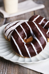 Delicious donuts with icing on plate on wooden background