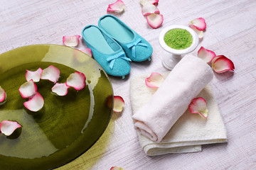 Spa bowl with water, rose petals, towel and slippers on light background. Concept of pedicure or natural spa treatment