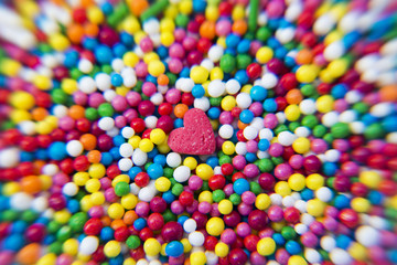 Fototapeta na wymiar Macro of Sugar Heart over colorfull balls powder background