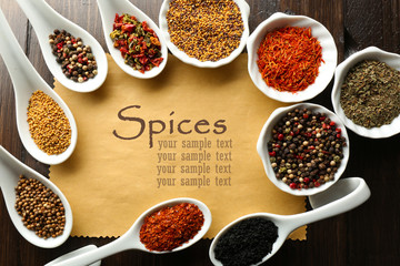 Different kinds of spices in bowls and spoons on blank paper sheet on wooden background