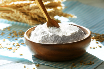 Bowl of flour with spoon and napkin on wooden table, closeup