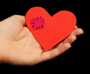 Obraz premium Female hand holding broken heart with patch on black background