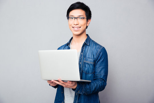 Cheerful asian man standing with laptop