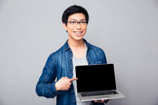 Smiling handsome asian man showing on laptop screen