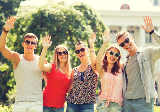 group of smiling friends waving hands outdoors