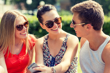 smiling friends with smartphone sitting in park