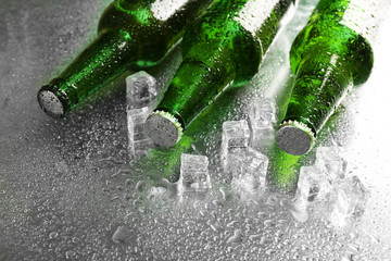 Glass bottles of beer with ice cubes on wet table background