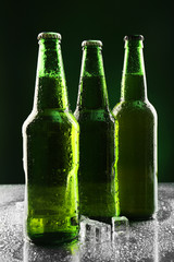 Glass bottles of beer with ice cubes on dark background