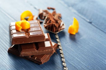 Pieces of chocolate with orange peels on color wooden