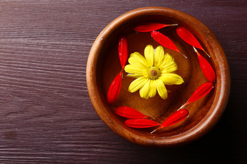 Flower petals in bowl, close-up, on wooden table background