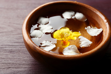Flower petals in bowl, close-up, on wooden table background