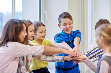 group of smiling school kids putting hands on top