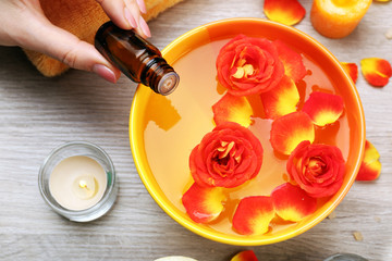 Female hand with bottle of essence and bowl of aroma spa water on wooden table, closeup