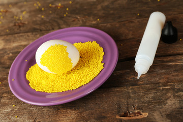 Decorating Easter egg on color plate on wooden table, closeup