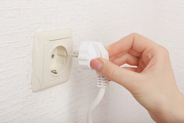 Hand putting plug in electricity socket close up