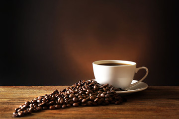 Cup of coffee with grains on wooden table on dark background
