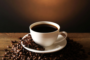 Cup of coffee with grains on wooden table on dark background